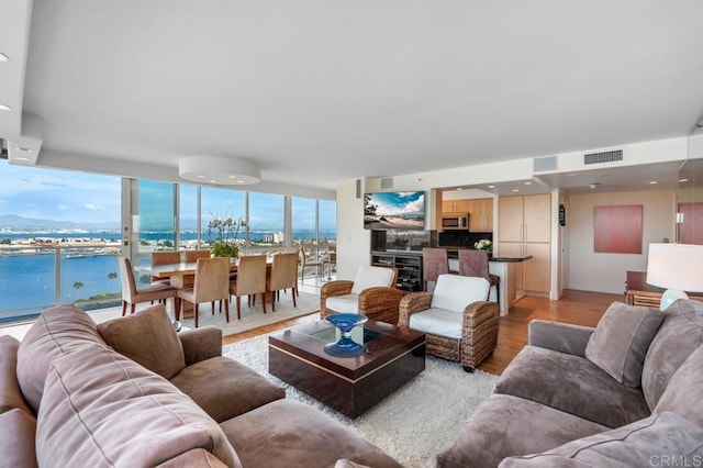 living area featuring expansive windows, light wood finished floors, visible vents, and a water view