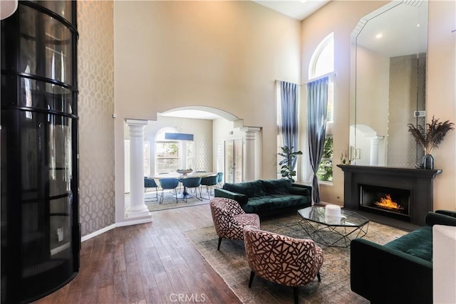 26962 Willow Tree Ln, Laguna Hills, CA 92653 - living area featuring arched walkways, decorative columns, a high ceiling, hardwood / wood-style floors, and a lit fireplace