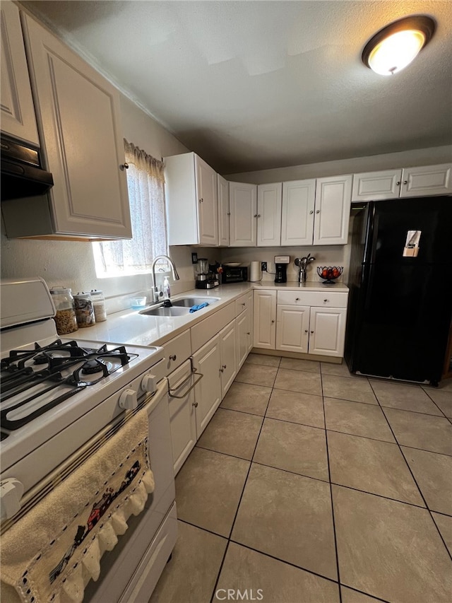 kitchen featuring light tile patterned floors, a sink, light countertops, freestanding refrigerator, and white range with gas cooktop