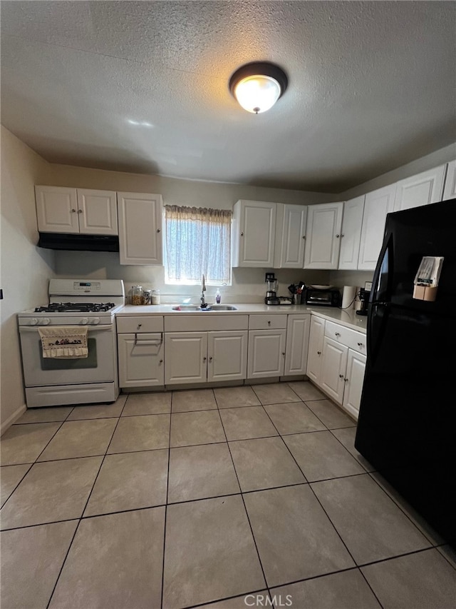 kitchen featuring a sink, light tile patterned floors, freestanding refrigerator, and white gas range