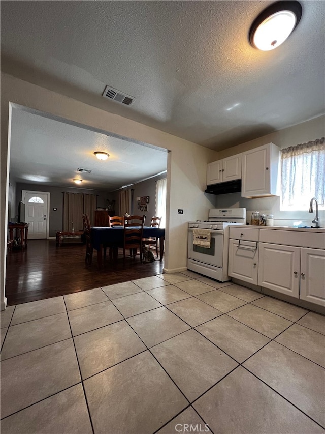 kitchen featuring white gas range oven, light tile patterned floors, under cabinet range hood, visible vents, and a sink
