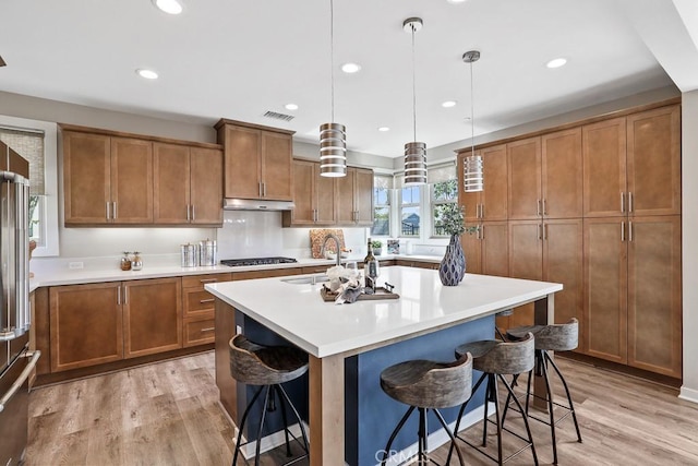 7 Alienta Ln, Rancho Mission Viejo, CA 92694 - kitchen with brown cabinets, a kitchen island with sink, light wood-style flooring, under cabinet range hood, and visible vents