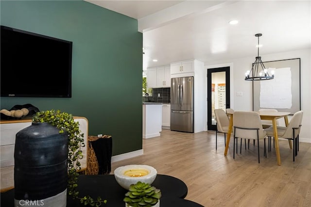 dining space featuring light wood-style flooring, baseboards, a notable chandelier, and beam ceiling