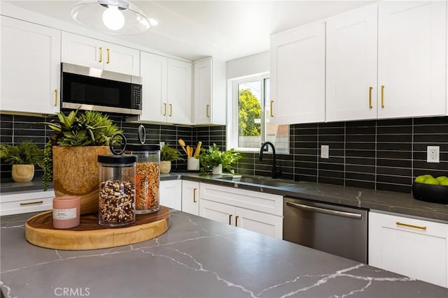 kitchen with dark stone countertops, white cabinetry, decorative backsplash, stainless steel appliances, and a sink