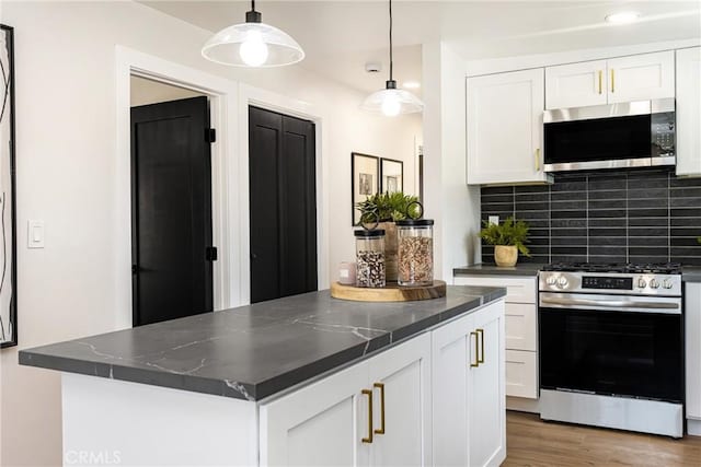 kitchen with dark countertops, appliances with stainless steel finishes, white cabinetry, wood finished floors, and decorative backsplash