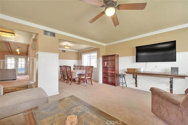 carpeted living room with crown molding, a ceiling fan, and visible vents