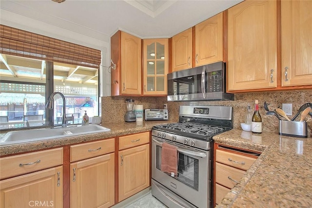 kitchen with glass insert cabinets, light brown cabinetry, a sink, stainless steel appliances, and decorative backsplash