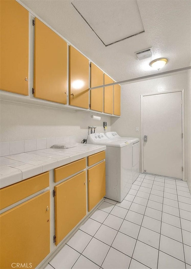 washroom featuring light tile patterned floors, a textured ceiling, visible vents, cabinet space, and washer and dryer