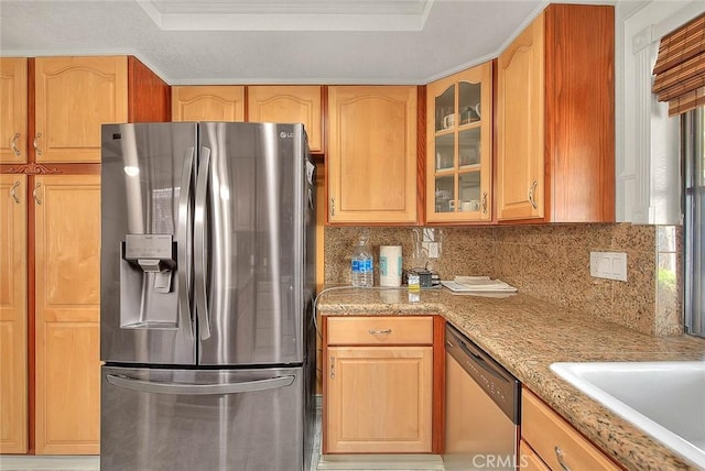kitchen with tasteful backsplash, glass insert cabinets, appliances with stainless steel finishes, a tray ceiling, and light stone countertops