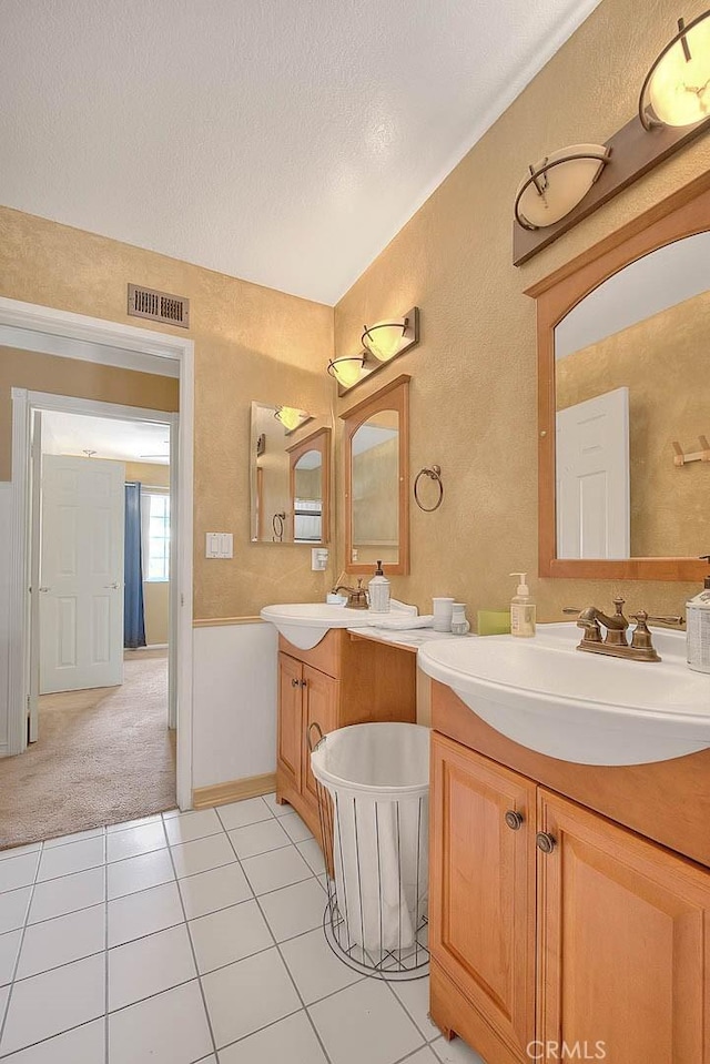 bathroom featuring two vanities, a textured ceiling, visible vents, a sink, and a textured wall