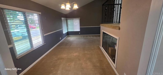 unfurnished living room with carpet flooring, a glass covered fireplace, baseboards, a notable chandelier, and lofted ceiling