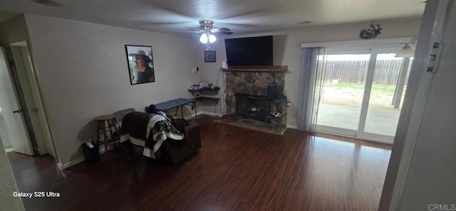 living room with baseboards, wood finished floors, a ceiling fan, and a stone fireplace