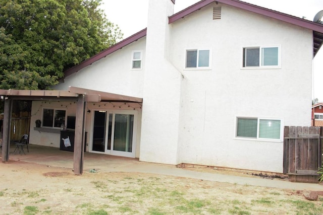 back of house featuring a patio, a chimney, stucco siding, and fence