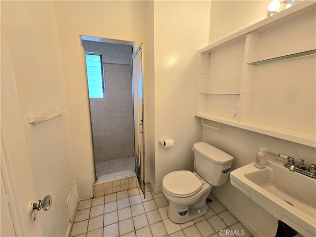 bathroom featuring a sink, baseboards, a tile shower, toilet, and tile patterned flooring