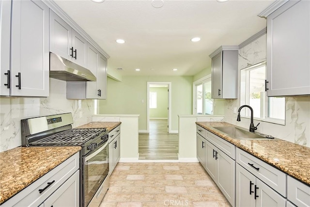 kitchen featuring tasteful backsplash, recessed lighting, under cabinet range hood, stainless steel gas range, and a sink