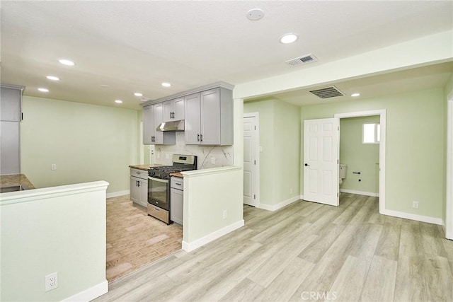 kitchen with under cabinet range hood, light wood finished floors, stainless steel gas range, and visible vents