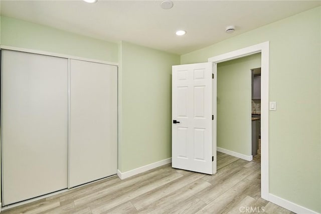 unfurnished bedroom featuring a closet, recessed lighting, light wood-style flooring, and baseboards