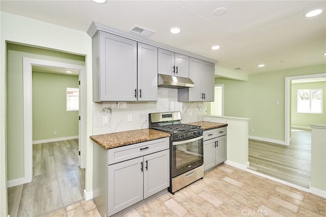kitchen with gray cabinets, backsplash, under cabinet range hood, visible vents, and stainless steel range with gas stovetop