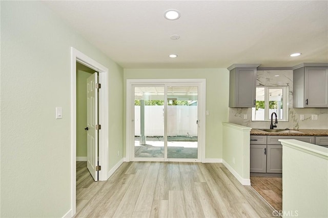 kitchen with a sink, gray cabinets, baseboards, and light wood-type flooring