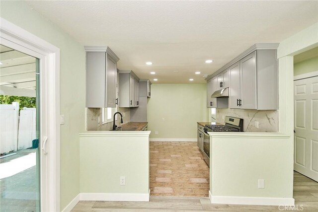 kitchen with under cabinet range hood, stainless steel gas stove, backsplash, and gray cabinets