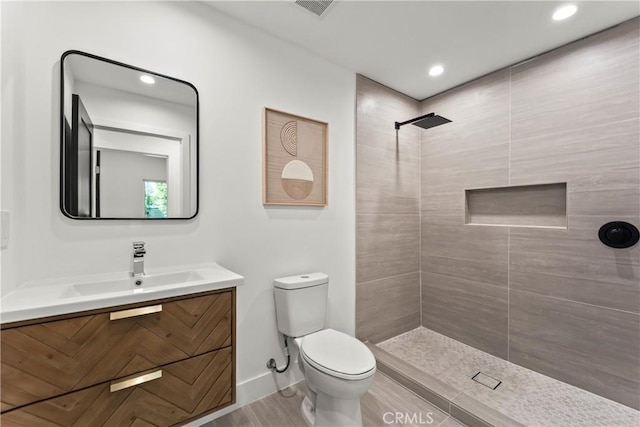 full bath with a tile shower, toilet, visible vents, recessed lighting, and vanity