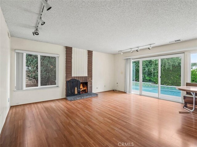 25582 Old Course Way, Valencia, CA 91355 - unfurnished living room with track lighting, wood finished floors, a brick fireplace, and a textured ceiling