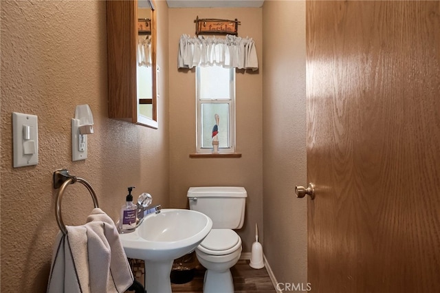 half bath featuring toilet, wood finished floors, a textured wall, and baseboards