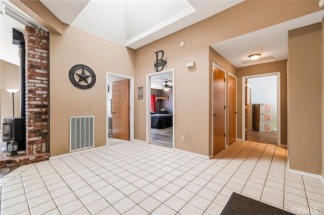 interior space featuring baseboards, light tile patterned floors, a wood stove, visible vents, and ceiling fan