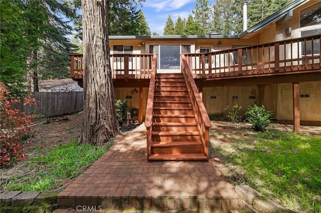 rear view of house with fence, a wooden deck, stucco siding, and stairs