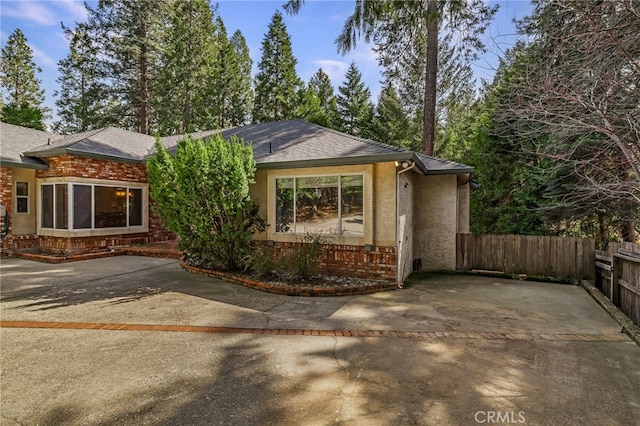 view of front of home with brick siding, roof with shingles, fence, and stucco siding