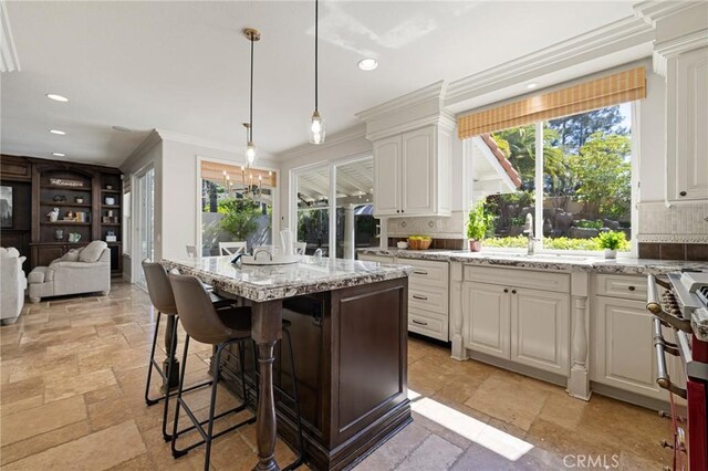 kitchen with stone tile floors, ornamental molding, a sink, and light stone counters