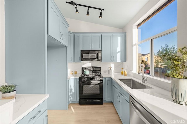 kitchen with a sink, light wood-type flooring, black appliances, vaulted ceiling, and light stone counters
