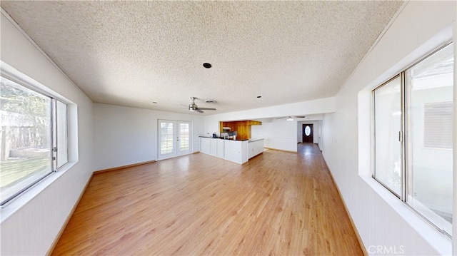unfurnished living room with light wood finished floors, a textured ceiling, baseboards, and ceiling fan