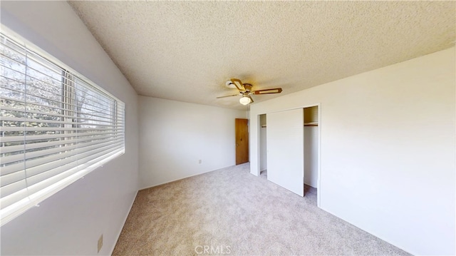 unfurnished bedroom with light carpet, a closet, a textured ceiling, and ceiling fan