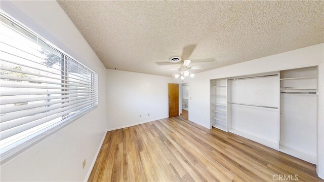 unfurnished bedroom with a closet, baseboards, light wood-type flooring, a textured ceiling, and visible vents