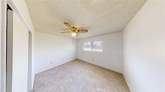 spare room with a ceiling fan, light colored carpet, and a textured ceiling