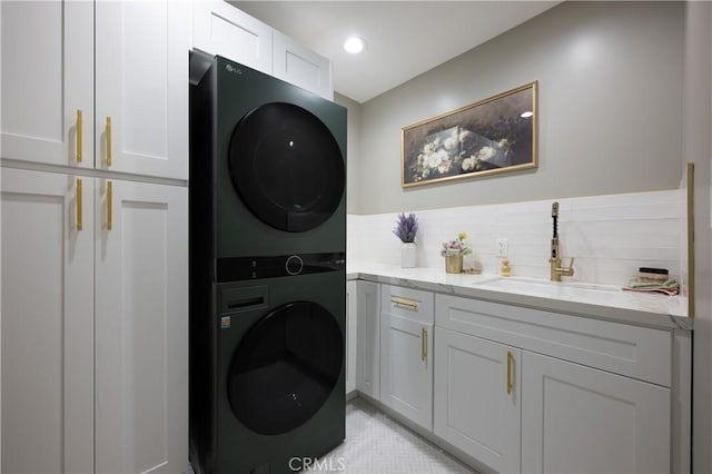 laundry room with stacked washer and clothes dryer, a sink, recessed lighting, and cabinet space