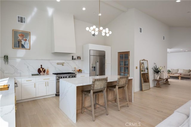 kitchen featuring high vaulted ceiling, premium appliances, light wood finished floors, white cabinets, and visible vents