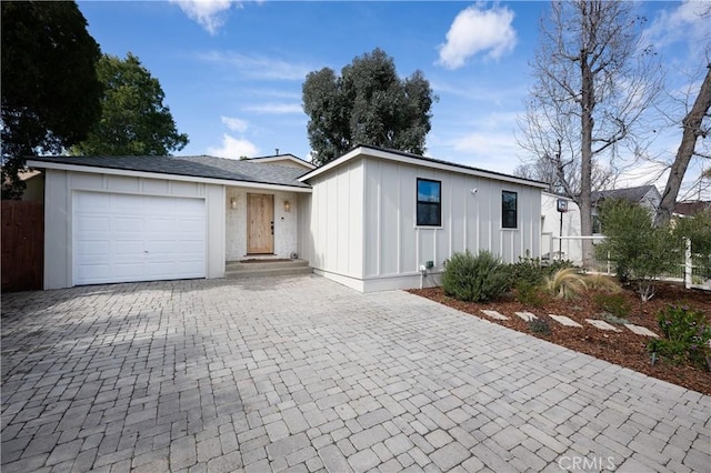 single story home with board and batten siding, an attached garage, decorative driveway, and fence