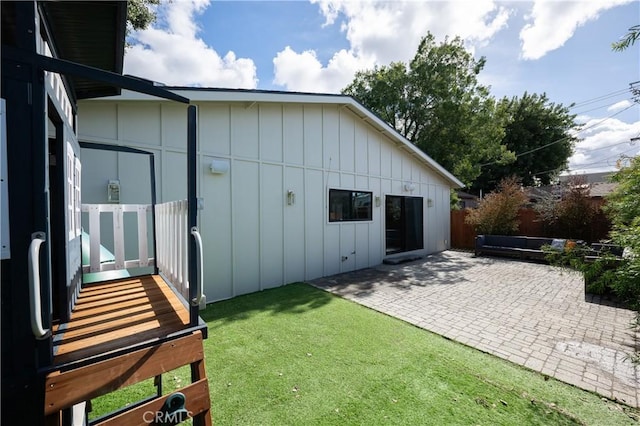 exterior space with board and batten siding, a patio area, fence, and a yard