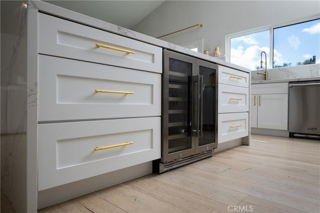 room details featuring white cabinets, a sink, light wood-type flooring, dishwasher, and beverage cooler