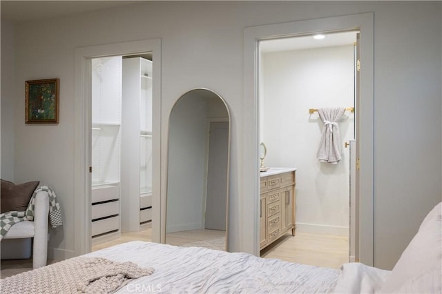 bedroom with arched walkways, baseboards, connected bathroom, and light wood-style floors