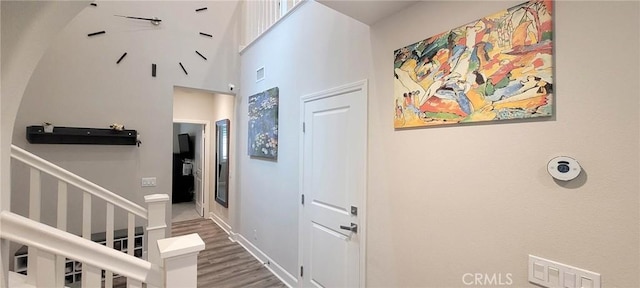 hallway featuring stairs, baseboards, wood finished floors, a towering ceiling, and visible vents