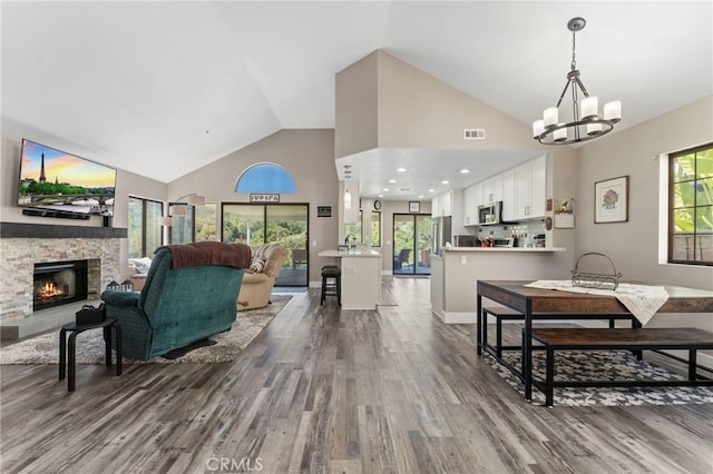 living room featuring a notable chandelier, a fireplace, high vaulted ceiling, wood finished floors, and visible vents