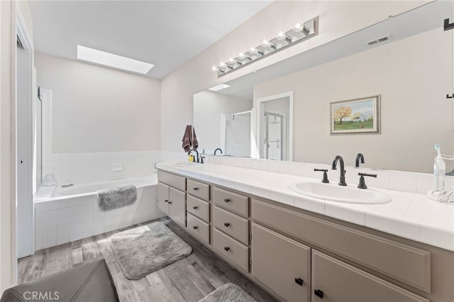 full bath featuring a skylight, visible vents, a sink, and wood finished floors