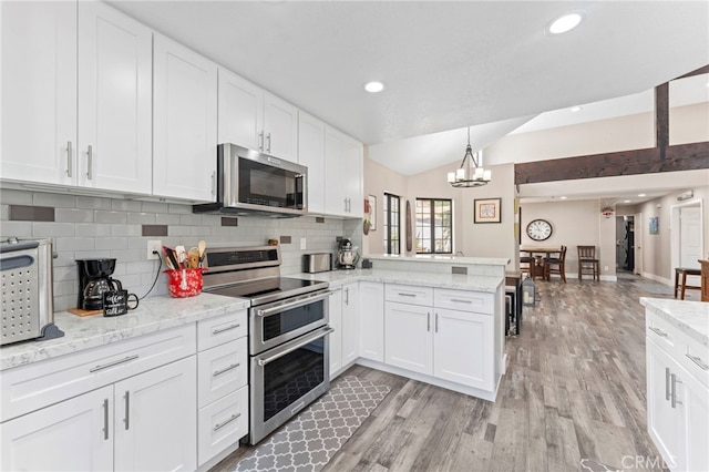 kitchen with a peninsula, appliances with stainless steel finishes, lofted ceiling, and tasteful backsplash