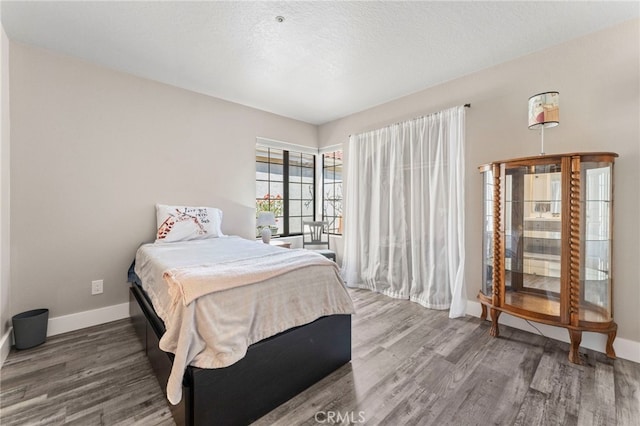 bedroom with baseboards, a textured ceiling, and wood finished floors