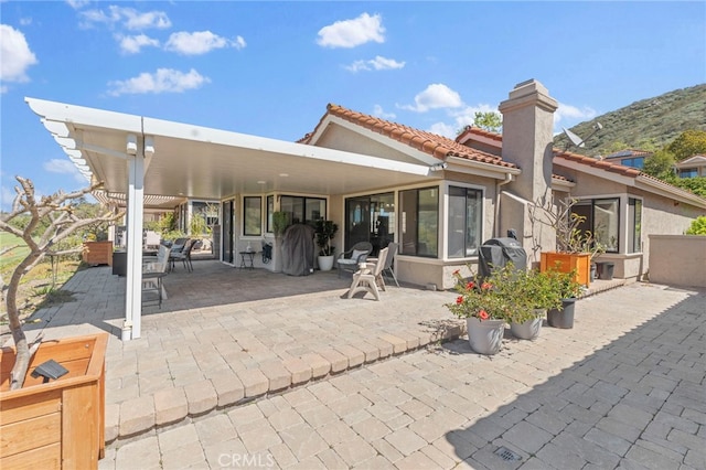 rear view of property featuring a tile roof, a chimney, a patio area, and stucco siding