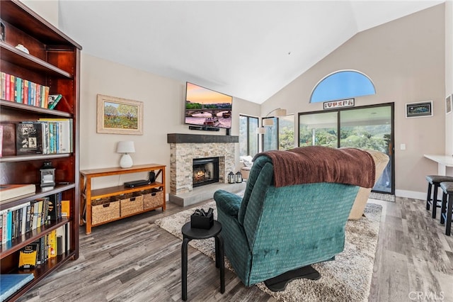 living area with baseboards, high vaulted ceiling, wood finished floors, and a fireplace