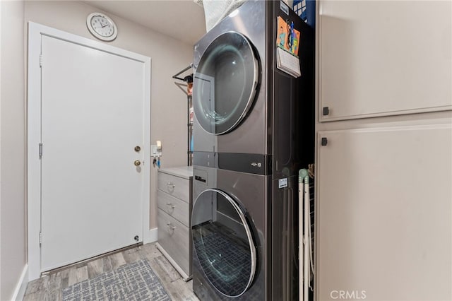 laundry area featuring light wood-style floors, baseboards, laundry area, and stacked washer / dryer